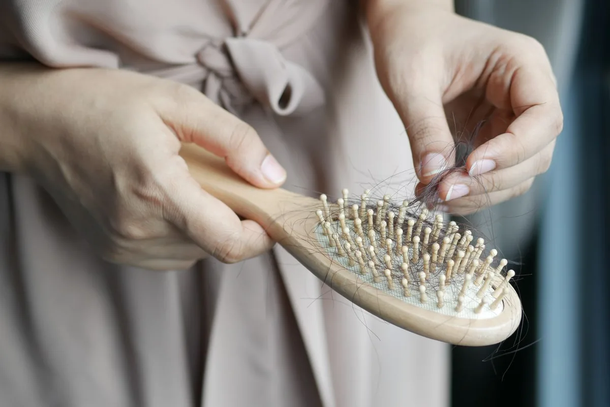 A woman's hands pulling shed hair out of a wooden hairbrush